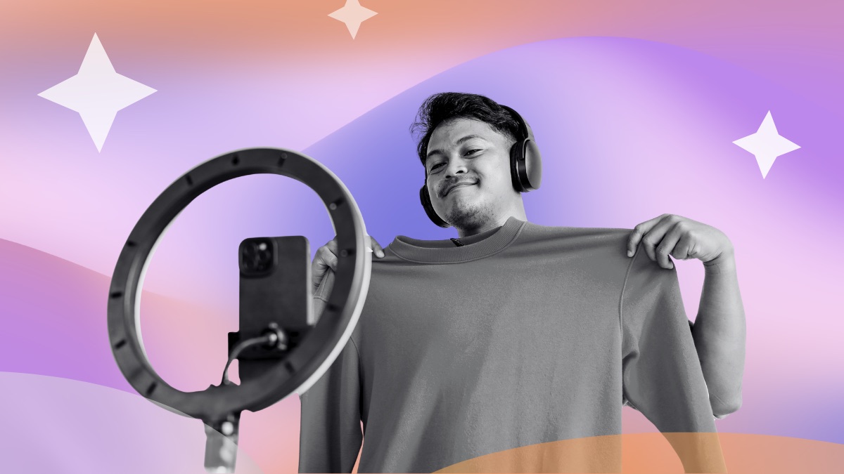 Man in headphones holding up a sweatshirt in front of a phone on a ring light, set against a pink and purple gradient with sparkle accents